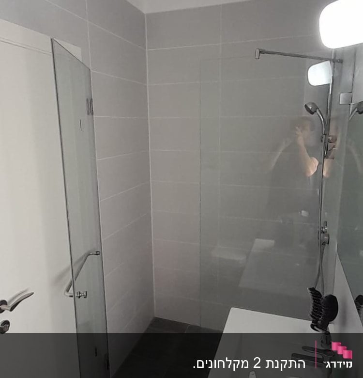 מקלחון זכוכית עם ראש מקלחת על קיר אריחים אפורים